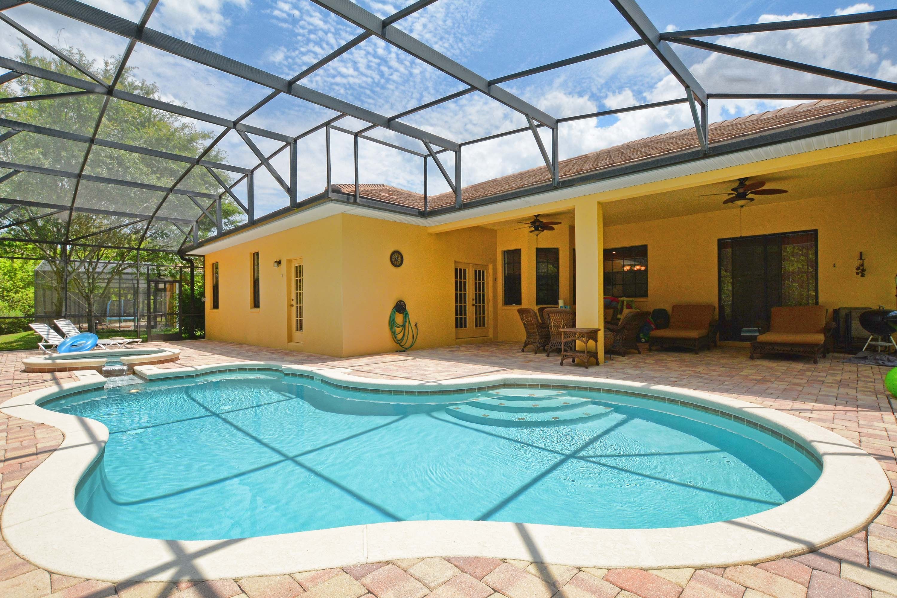 Una piscina con cerramiento de vidrio, un porche cubierto con mobiliario y vistas al exterior.