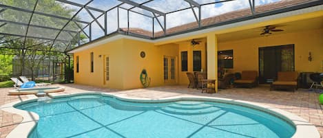 Una piscina con cerramiento de vidrio, un porche cubierto con mobiliario y vistas al exterior.
