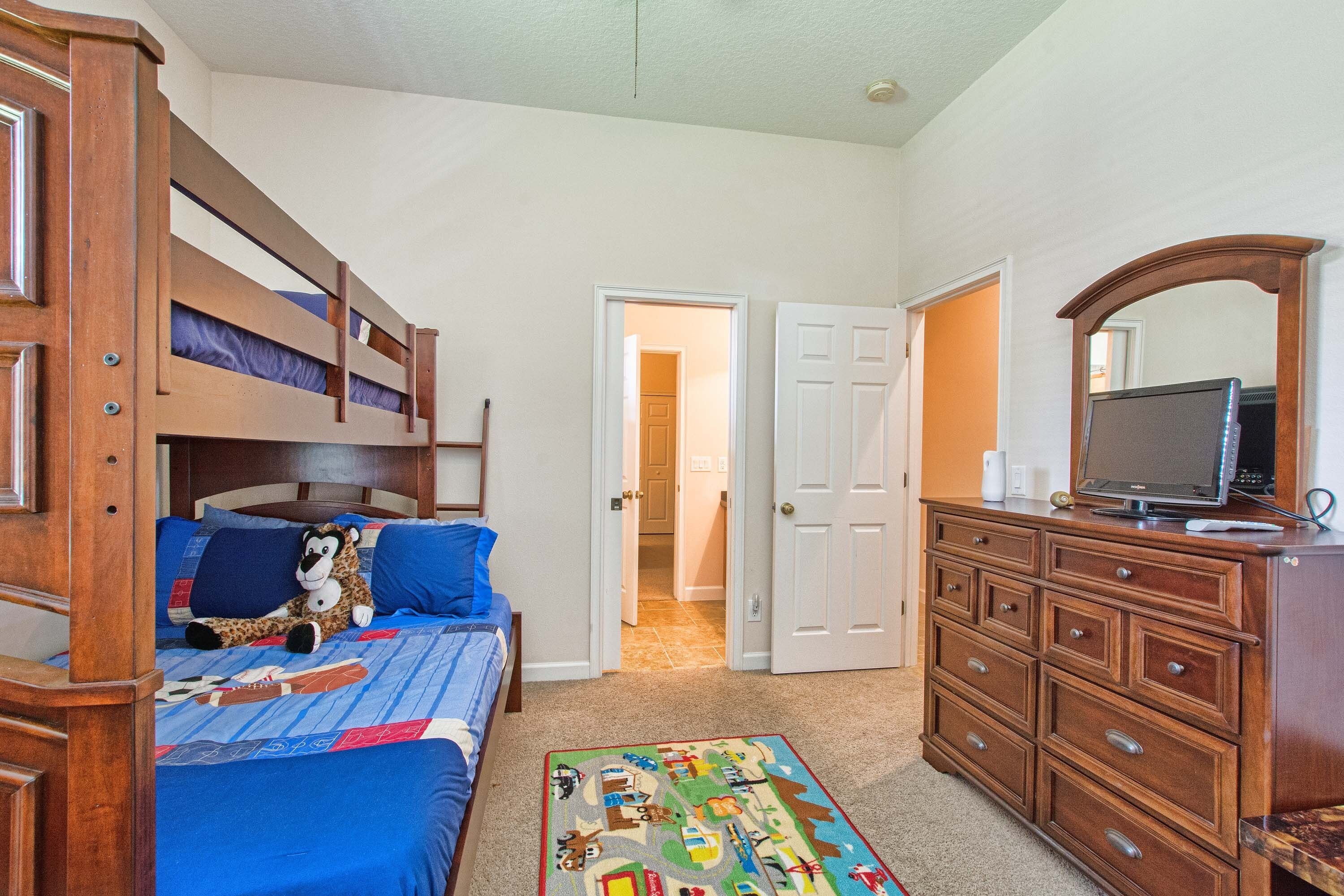 A bedroom with a bunk bed, a dresser, a television, and a door leading to another room.