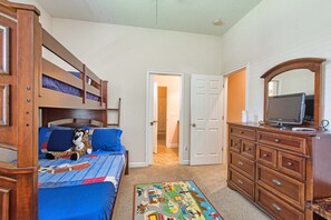 Un dormitorio con literas, un aparador, un televisor y una puerta que da a otra habitación.