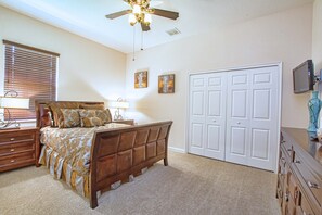 Ein Schlafzimmer mit Bett, Kommode, Nachttisch, Lampe, Deckenventilator, Kunstwerk und einer Tür.