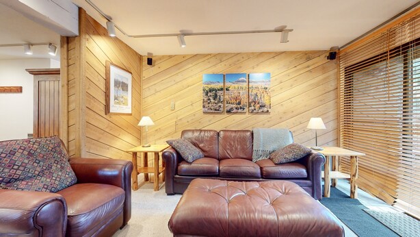 A cozy living room with a wooden paneled wall, a brown leather sofa, a matching ottoman, and a small wooden side table with a lamp. - Wildflower #51 1 Bedroom Condo by RedAwning (Mammoth Lakes)