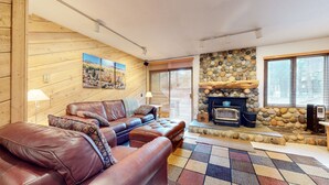 A cozy living room with a stone fireplace, wooden walls, and a leather sofa.