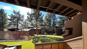 A wooden deck with a view of a grassy courtyard and buildings in the background. - Wildflower #51 1 Bedroom Condo by RedAwning (Mammoth Lakes)
