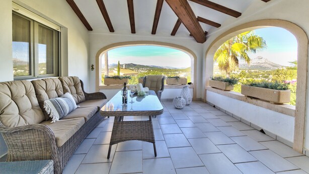 Un patio iluminado por el sol con un sofá, una mesa y sillas, con vistas a un paisaje pintoresco con montañas y un volcán.