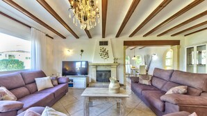 Amplia sala de estar con dos sofás, chimenea, televisor y candelabro.