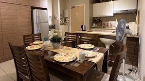 A dining area with a wooden table, chairs, and a flower centerpiece. There is a kitchen in the background with cabinets and appliances. - Premium Retreat Suite Icon City (Petaling Jaya)