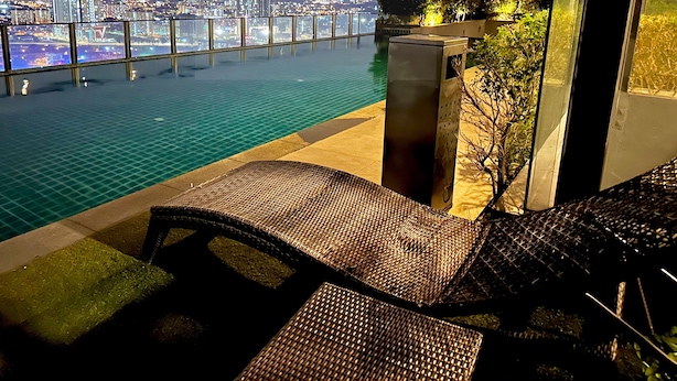 A balcony with a view of a cityscape at night, a pool, and wicker furniture. - Premium Retreat Suite Icon City (Petaling Jaya)