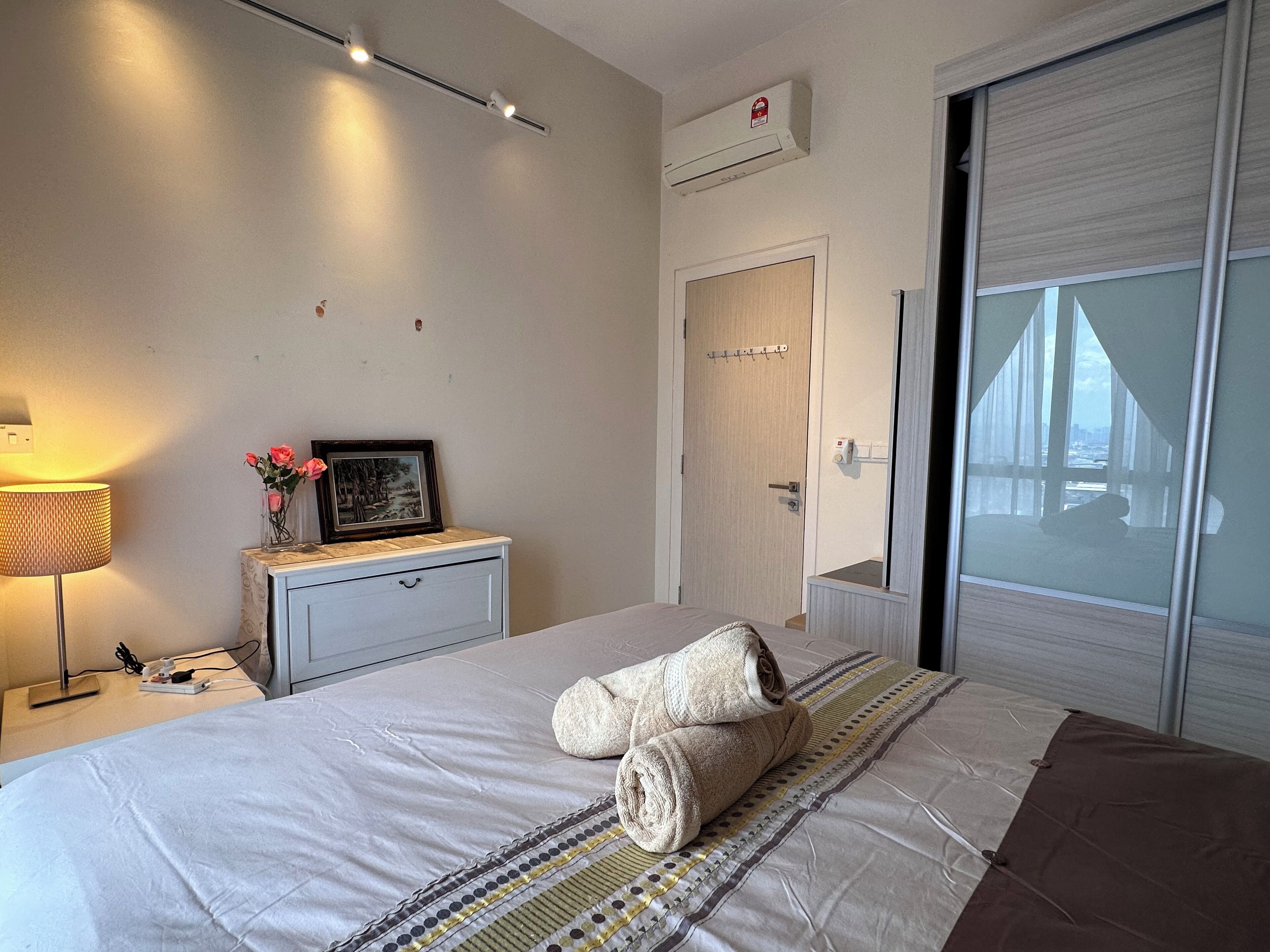 Una habitación de hotel con cama, una mesita de noche con lámpara, un marco de foto y vistas a un puente desde la ventana.
