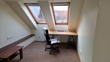 A small, sloped room with a desk, chair, and bench. There are two windows providing natural light.