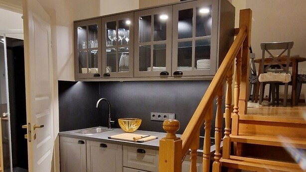 A modern kitchen with grey cabinets, a wooden staircase, and a dining area with a chandelier. - TyzenXL Luxury Vilnius Apartment (Vilnius)