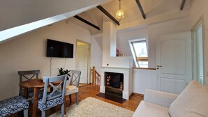 A loft-style living room with a fireplace, a television mounted on the wall, and a skylight. - TyzenXL Luxury Vilnius Apartment (Vilnius)