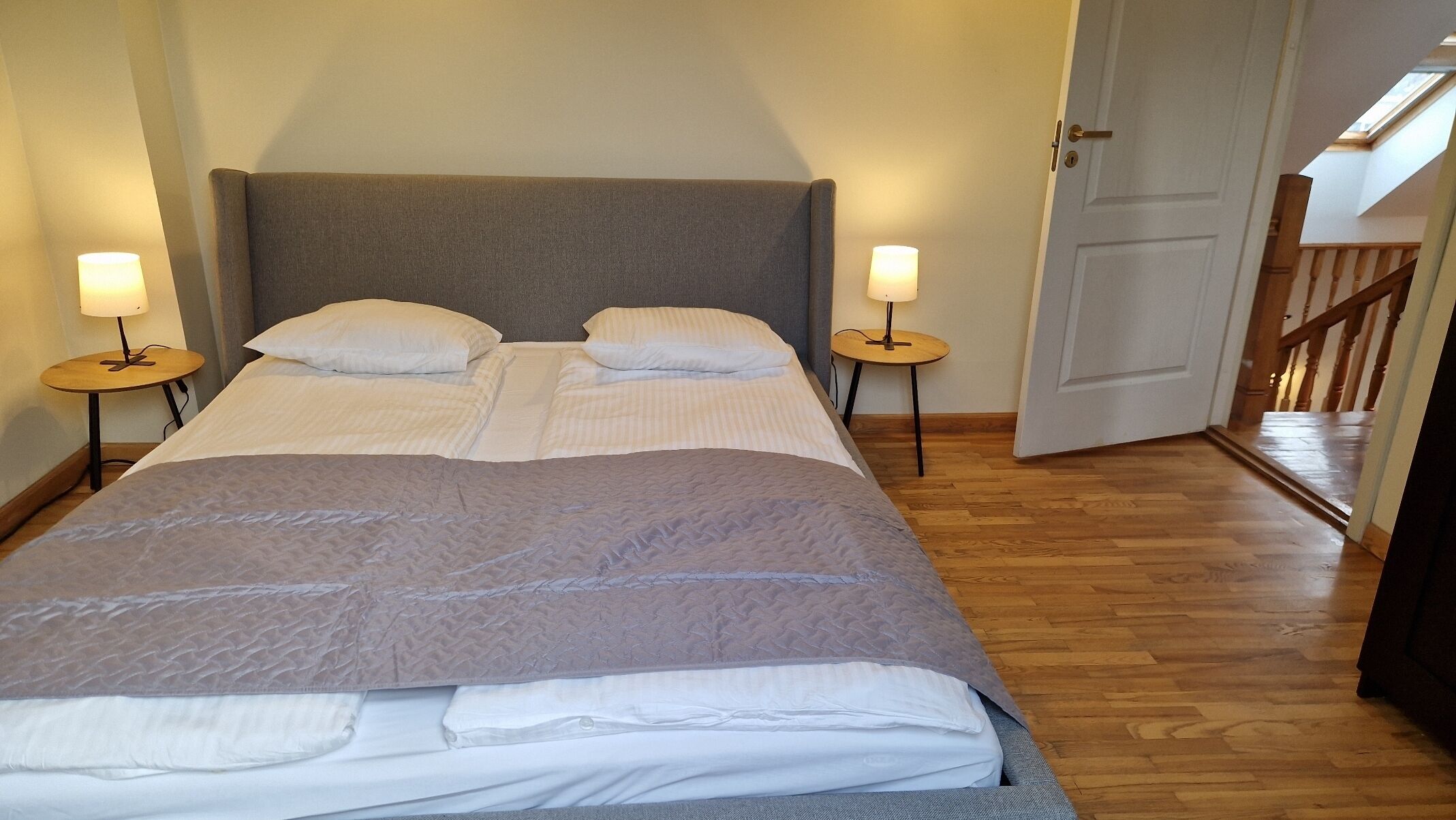 A double bed with a grey headboard, two bedside tables with lamps, and a wooden floor.