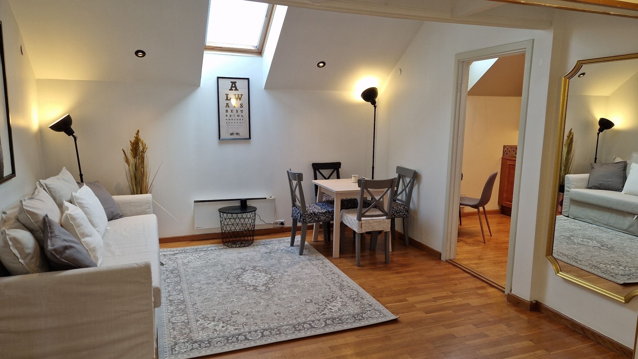 A cozy living room with a sofa, a dining table with chairs, a patterned rug, and a ceiling light.