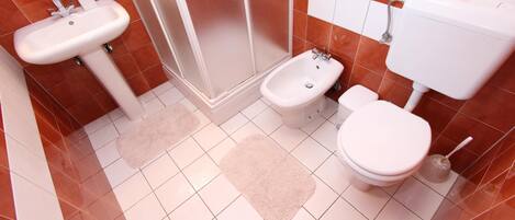 A bathroom with a sink, bidet, toilet, and a shower area.