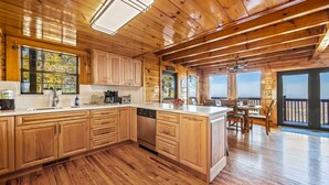 Une cuisine rustique aménagée dans une cabane en bois, avec un grand îlot central, des meubles de rangement en bois et un coin repas offrant une vue agréable.