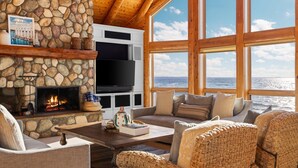 A cozy living room with a stone fireplace, comfortable seating, a flat-screen TV, and large windows overlooking the ocean.