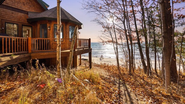 A wooden cabin with a deck overlooking a beach and ocean.