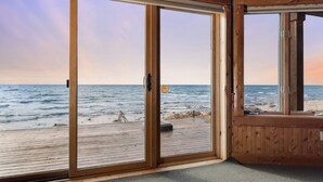 A room with large sliding glass doors leading to a wooden deck overlooking a beach.