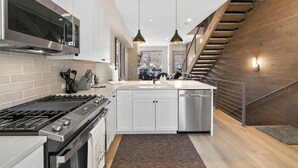 A modern kitchen with stainless steel appliances, a central island, and a wooden staircase. - Private Rooftop Balcony w/ Hot Tub & Panoramic Mountain Views, Close to Shops (Silverthorne)