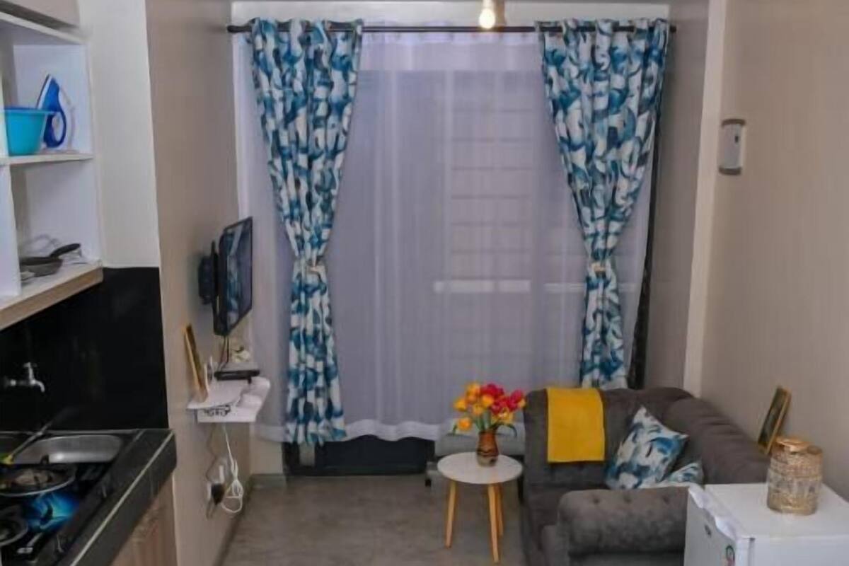 Habitación de hotel compacta con kitchenette, un sofá, una cama y una pequeña mesa con flores.