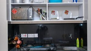 A kitchen with a microwave, toaster, and various kitchen utensils on the upper shelf. Below, there is a stove with a gas burner and a sink.