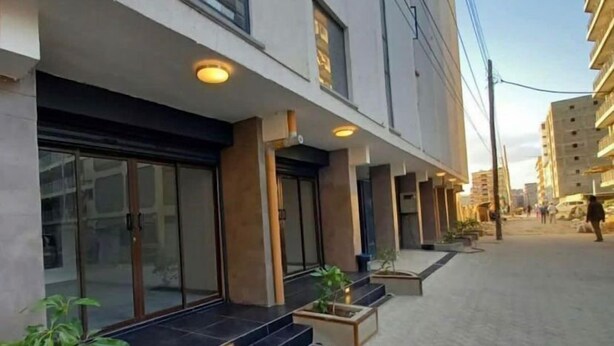 A modern building with a paved entrance, large windows, and outdoor plants.