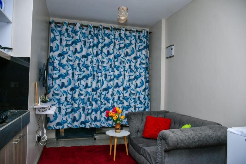 A living room with a grey sofa, a red rug, and a small white table with a vase of flowers.