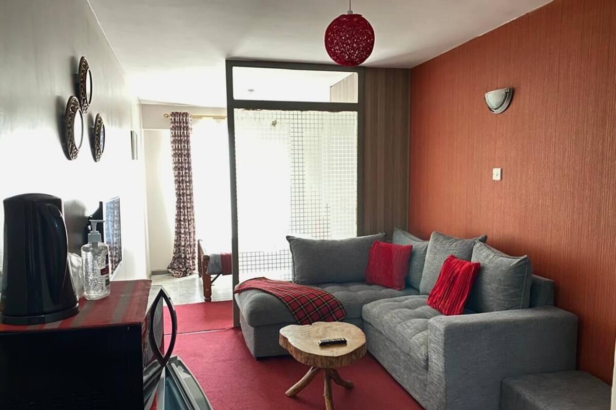Una sala de estar moderna con un sofá gris, cojines rojos, una mesita de centro de madera y una lámpara colgante roja.