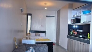 A compact hotel room with a bed, a sofa, a kitchenette, and a small dining area.