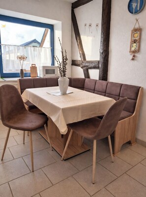 Ein Essbereich mit einem Tisch für vier Personen, einer braunen Couch und einer Vase mit Zweigen.