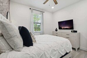 A bedroom with a bed, a dresser, a television, and a window with curtains.