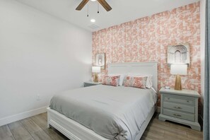 A bedroom with a large bed, two bedside tables with lamps, a ceiling fan, and patterned wallpaper. - Golf Course Views, Private Pool & Pet-Friendly (Bonita Springs)