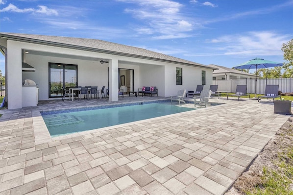 A modern outdoor pool area with a covered patio, seating, and a barbecue setup.