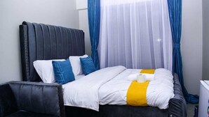 A neatly made bed with white and blue bedding, a black headboard, and a yellow accent. - Lux Suites Convertible Studios Embakasi (Nairobi)