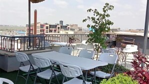 An outdoor patio with tables and chairs, surrounded by greenery and overlooking a cityscape. - Lux Suites Convertible Studios Embakasi (Nairobi)