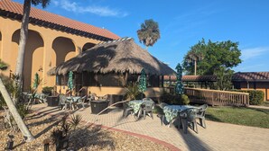 A patio area with tables and chairs, a thatched-roof structure, and a palm tree. - Marina Fish- Boat and Relax in this Paradise newly remodeled in Naples, Florida! (Naples)