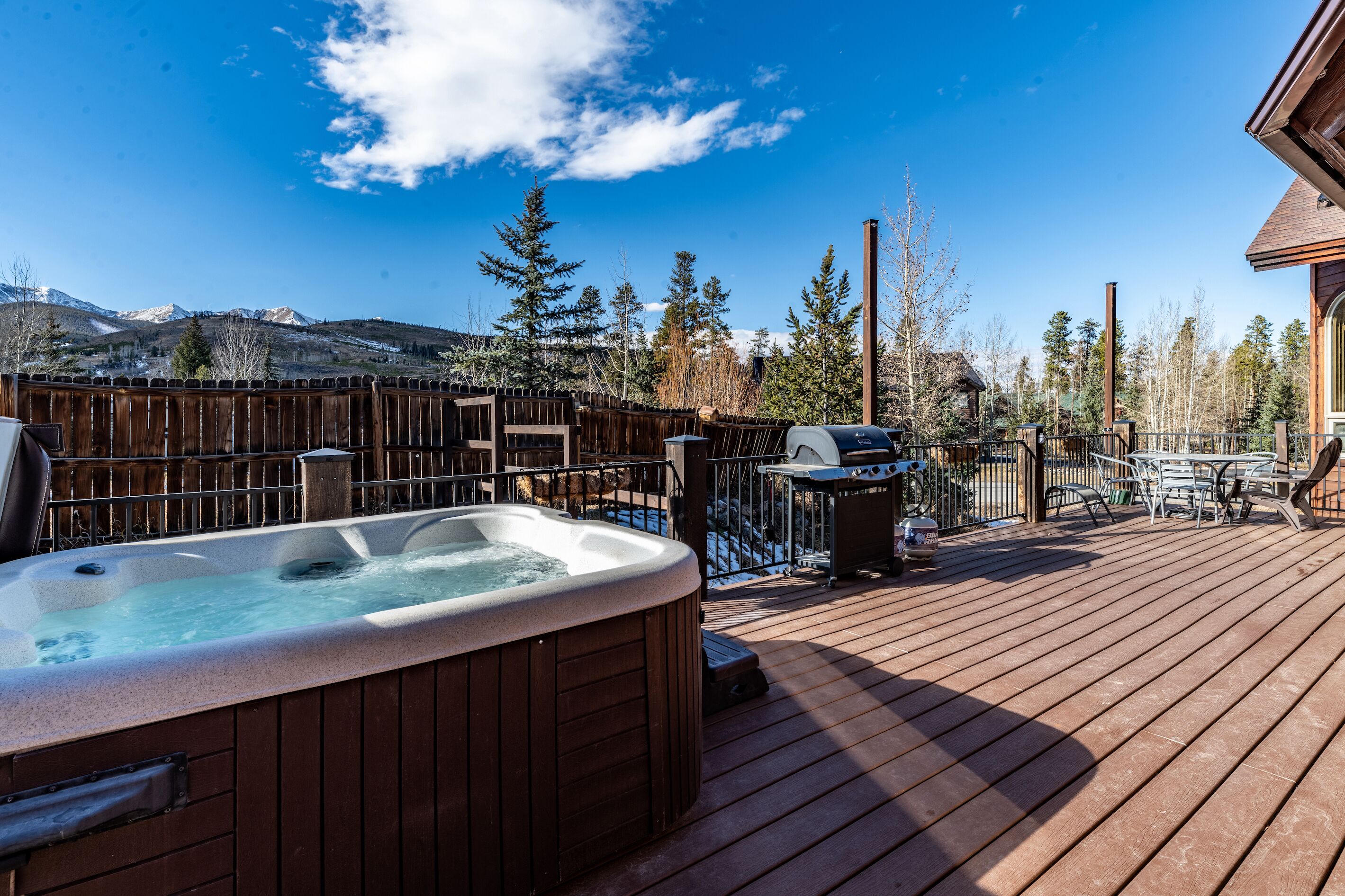 A wooden deck with a hot tub, outdoor furniture, and a view of mountains.