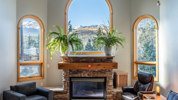 Una sala de estar acogedora con chimenea de piedra, amplias ventanas arqueadas y vistas a las montañas.