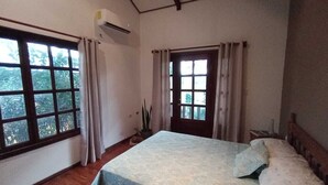 A bedroom with a bed, two windows, a door, and an air conditioning unit. - Casa Bugambilia

 (Bejuco)