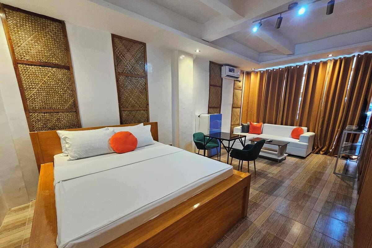A modern hotel room with a large bed, a sofa, a small table, and a TV.