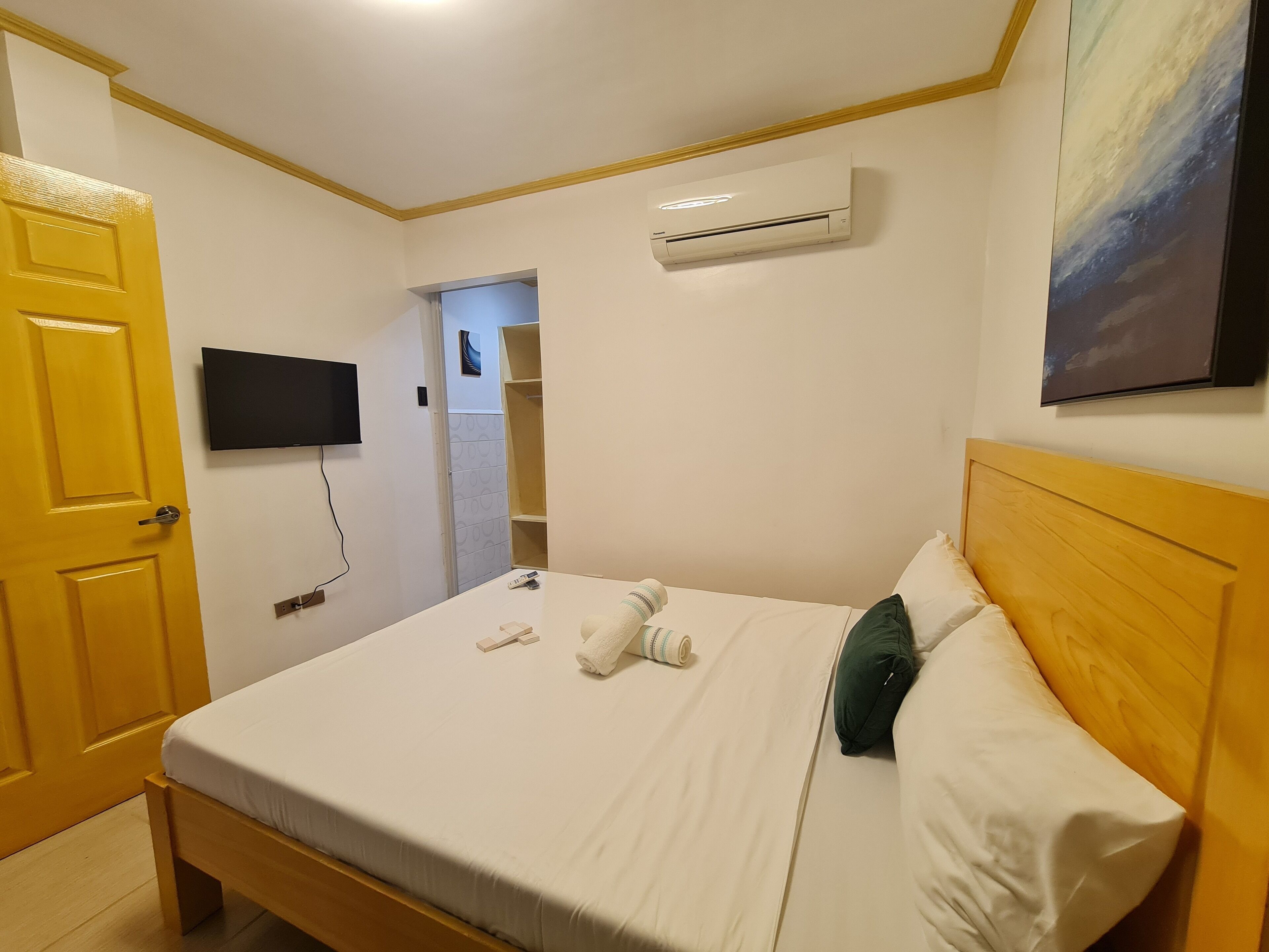 Een hotelkamer met een bed, een televisie, airconditioning en een schilderij aan de muur.