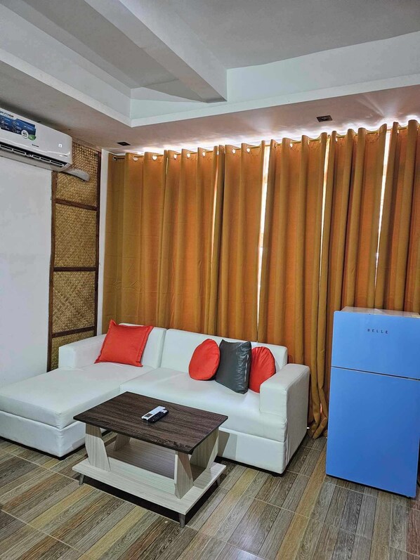 A modern living room with a white sofa, red and black cushions, a wooden coffee table, and a blue refrigerator.