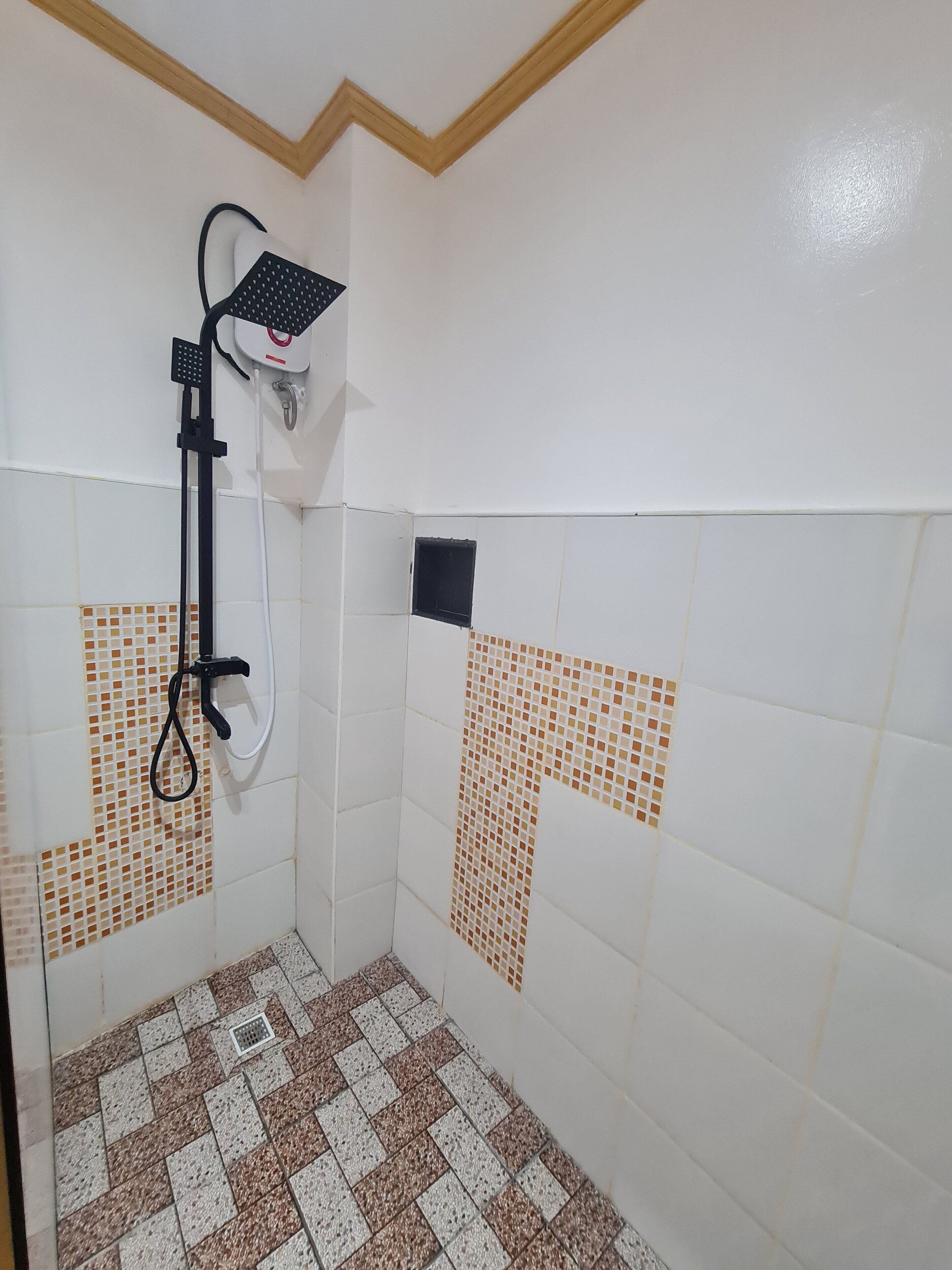 A small, tiled shower area with a handheld showerhead and a wall-mounted faucet.
