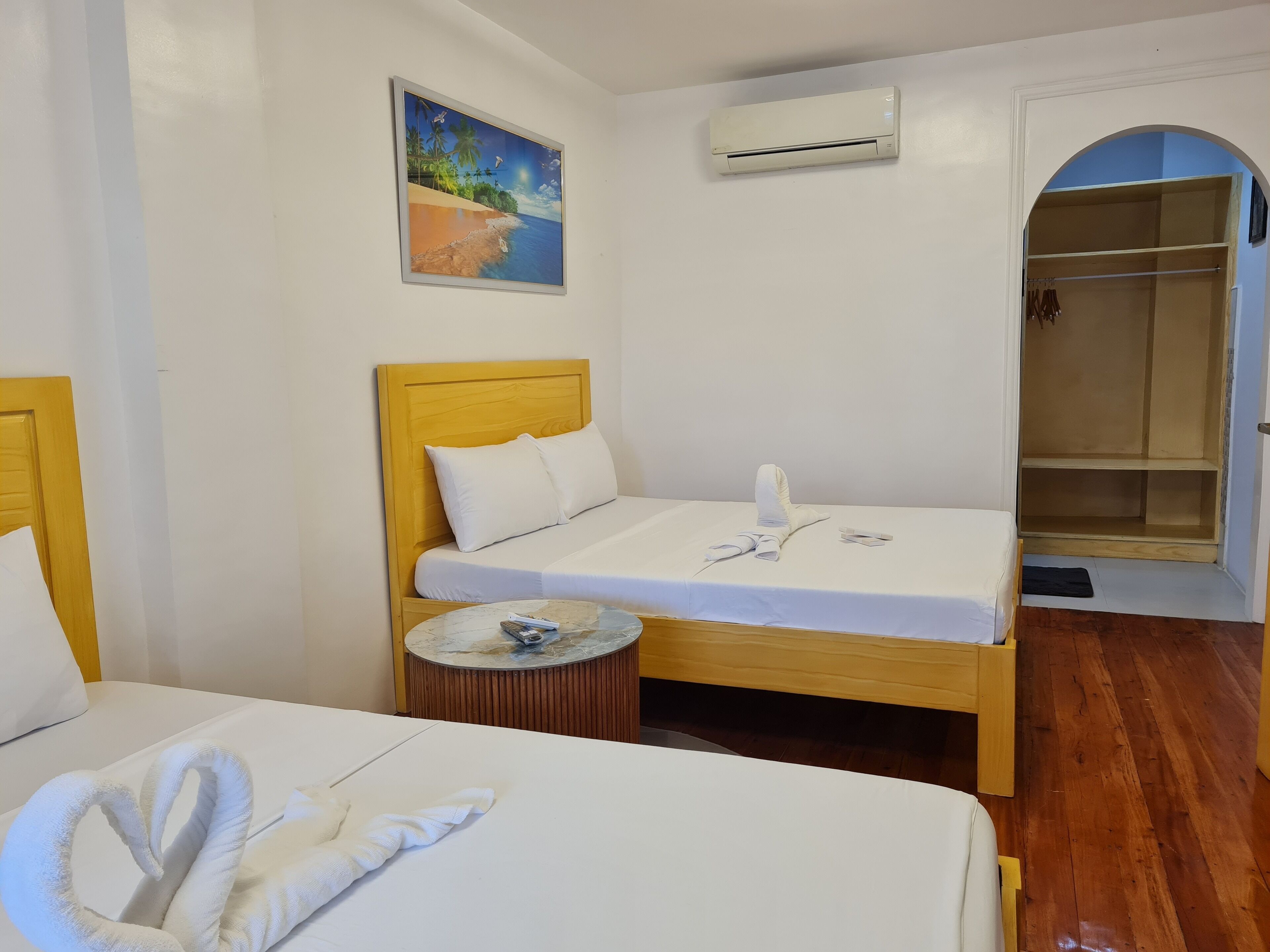 A hotel room with a bed, a bedside table, a towel, a painting, and an air conditioning unit.