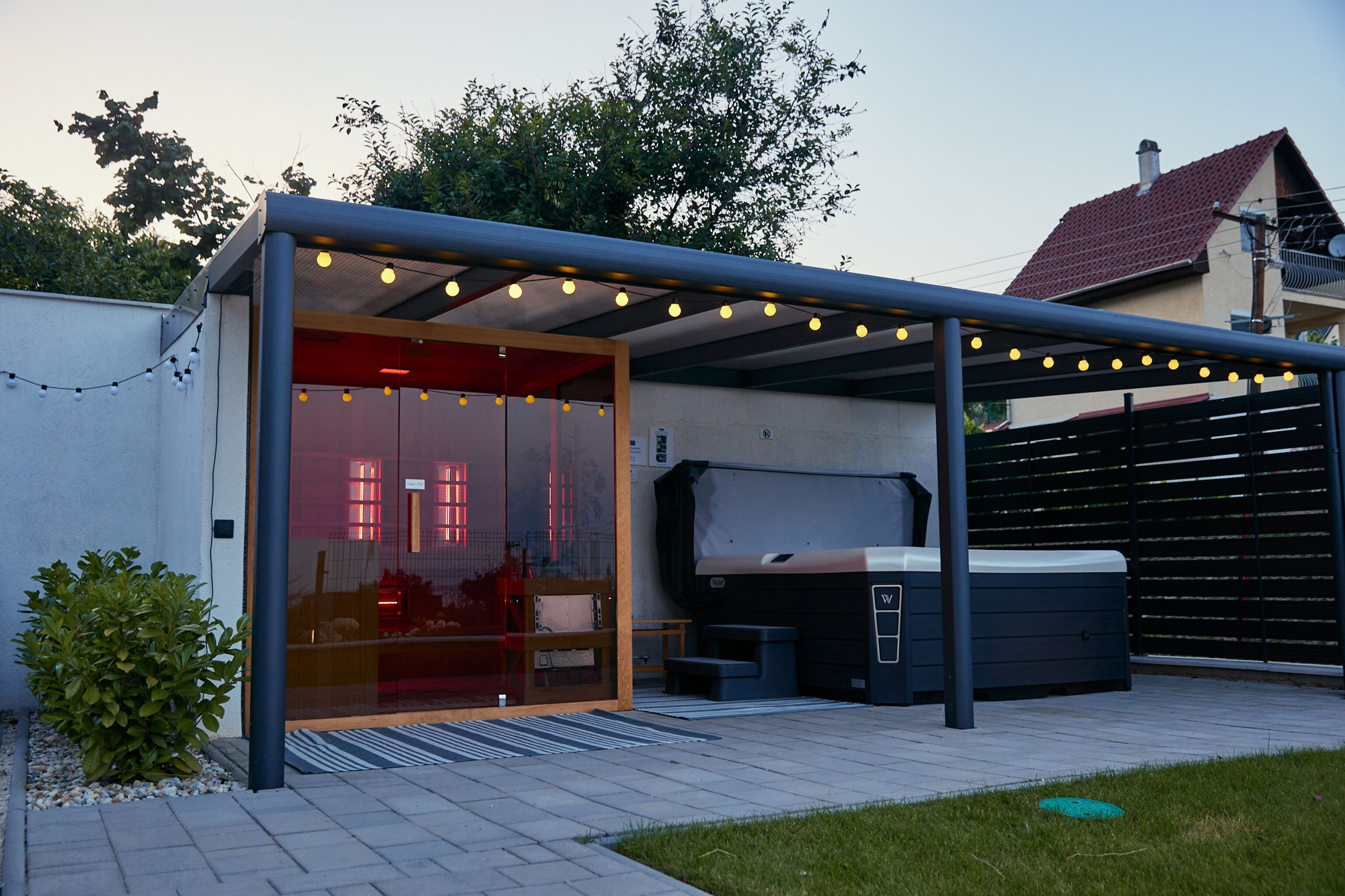 A covered outdoor area with a hot tub, a glass door entrance, and string lights.