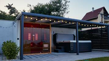 A covered outdoor area with a hot tub, a glass door entrance, and string lights.