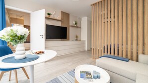 A modern living room with a flat-screen TV, a sofa, a dining table with a vase of flowers, and a wooden partition. - Lake Spirit Boutique Apartments (Balatonalmadi)