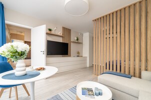 Uma sala de estar moderna com uma TV de tela plana, um sofá, uma mesa de jantar com um vaso de flores e um divisório de madeira.
