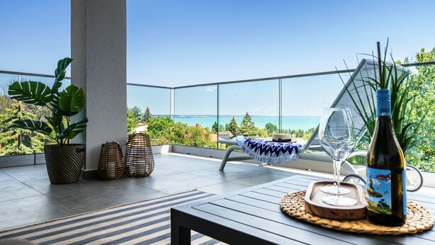 A balcony with a view of the ocean, a table with a bottle, and two chairs. - Lake Spirit Boutique Apartments (Balatonalmadi)